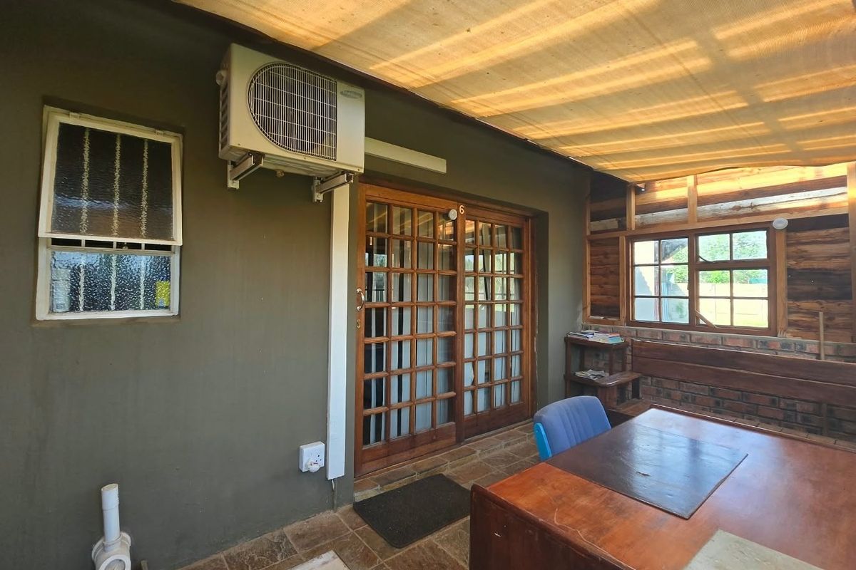 Covered patio area featuring a shade cloth canopy, timber-framed sliding doors, and an installed air conditioning unit, offering a functional outdoor living space.