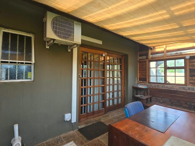 Covered patio area featuring a shade cloth canopy, timber-framed sliding doors, and an installed air conditioning unit, offering a functional outdoor living space.