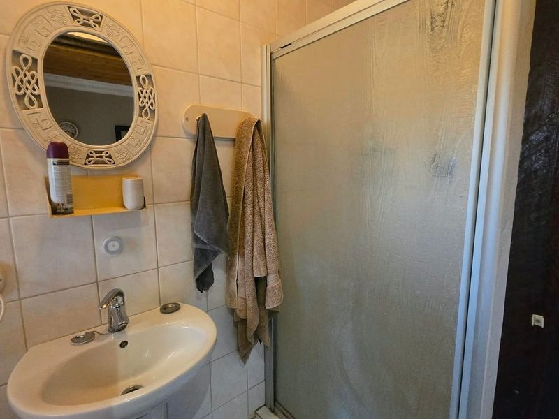 A functional bathroom featuring a wall-mounted basin with chrome mixer tap and a separate shower enclosure with tiled walls.
