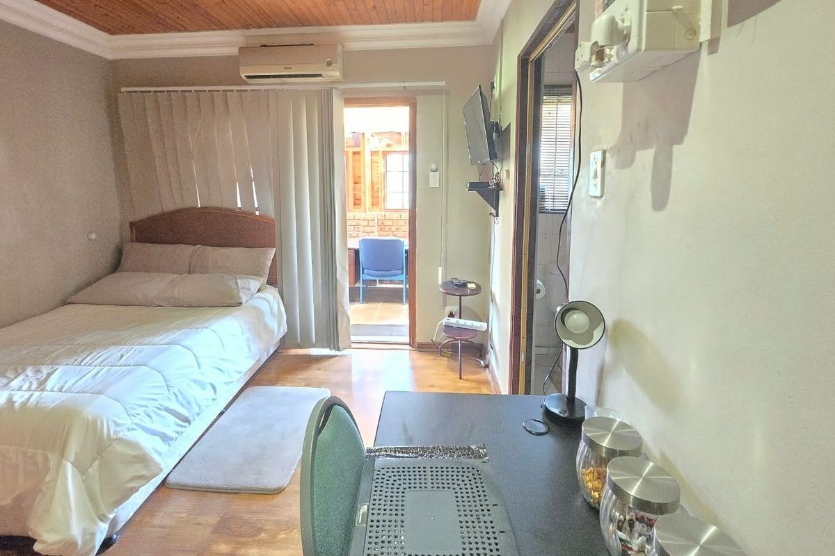 A bedroom featuring timber ceilings, laminate flooring, and an integrated air conditioning unit, with direct access to an outdoor patio area.