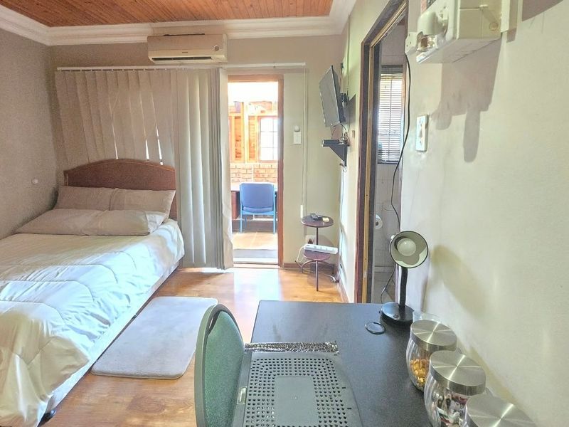 A bedroom featuring timber ceilings, laminate flooring, and an integrated air conditioning unit, with direct access to an outdoor patio area.