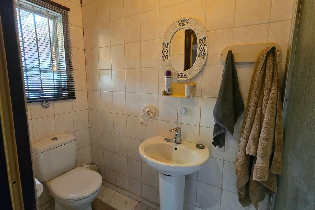 A functional bathroom featuring a pedestal basin, toilet, and tiled wall finishes, providing a practical space with natural light from the window.