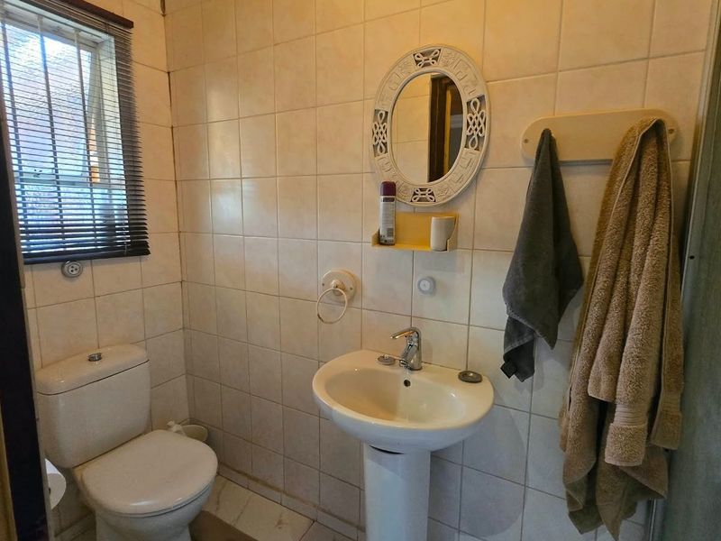 A functional bathroom featuring a pedestal basin, toilet, and tiled wall finishes, providing a practical space with natural light from the window.