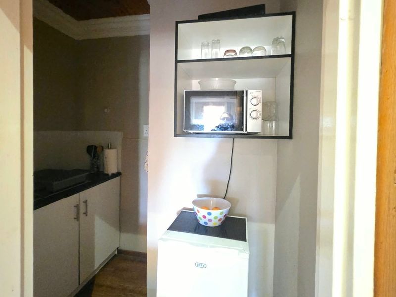A compact scullery or kitchenette area featuring built-in cabinetry, a laminate countertop, and a wall-mounted microwave shelf.