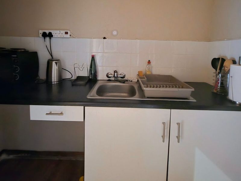 A compact kitchen area featuring a stainless steel sink, tiled splashback, laminate countertop, and basic built-in cabinetry.