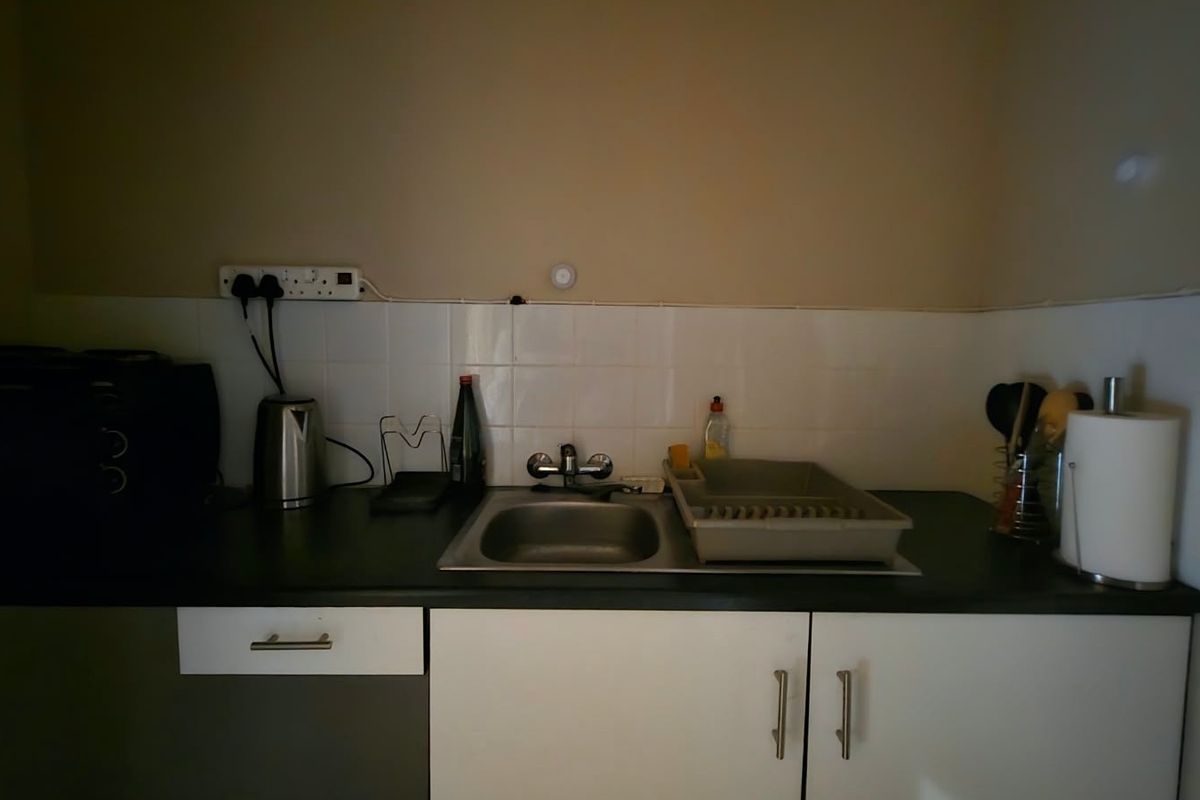 A compact kitchen area featuring a stainless steel sink, tiled splashback, and functional base cabinetry with laminate countertops.