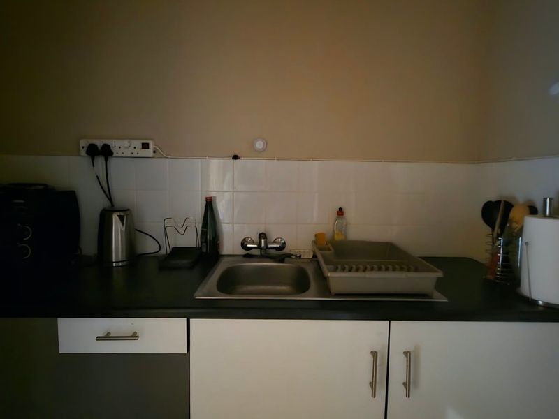 A compact kitchen area featuring a stainless steel sink, tiled splashback, and functional base cabinetry with laminate countertops.