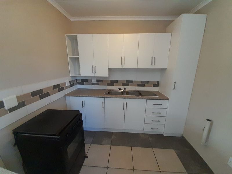 A clean and functional kitchen featuring white built-in cabinetry, a double bowl sink, tiled backsplash, and neutral floor tiles.