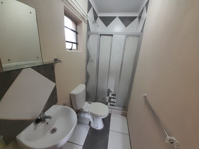 A functional bathroom featuring a pedestal basin, toilet, and a glass-enclosed shower with decorative tiled accents.