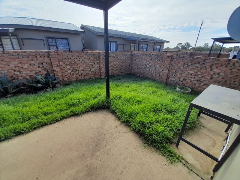 A private rear garden area featuring a concrete patio, lawn, and enclosed by a brick boundary wall.