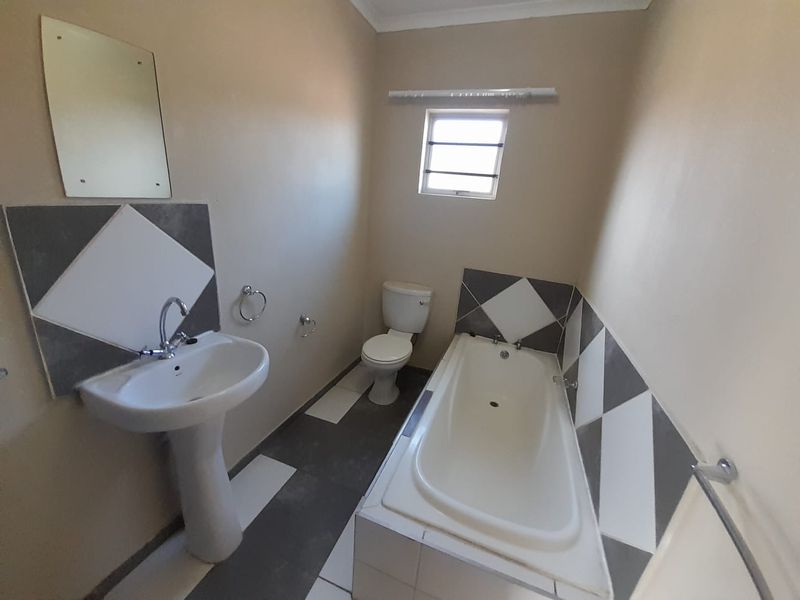 A functional bathroom featuring a pedestal basin, built-in bathtub, and toilet with neutral wall finishes and diamond-patterned tiled splashbacks.