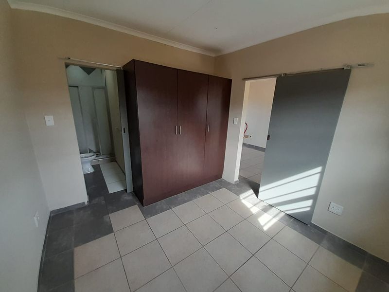 A functional bedroom featuring tiled flooring, a built-in wardrobe, and direct access to an en-suite bathroom.