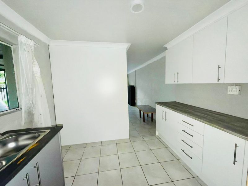A functional kitchen area featuring white built-in cabinetry, laminate countertops, a stainless steel sink, and neutral tiled flooring.