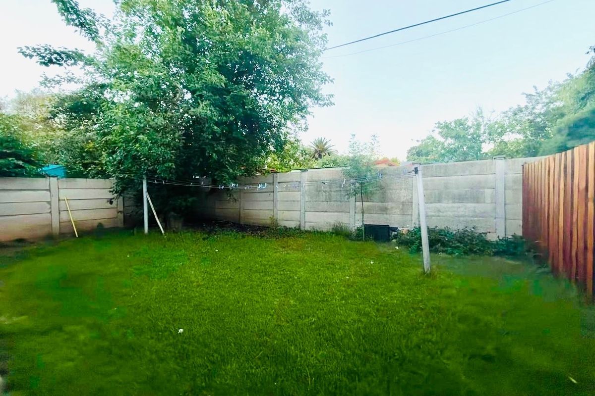 A private backyard garden featuring a lawn, mature tree, and a combination of precast concrete and wooden boundary fencing.