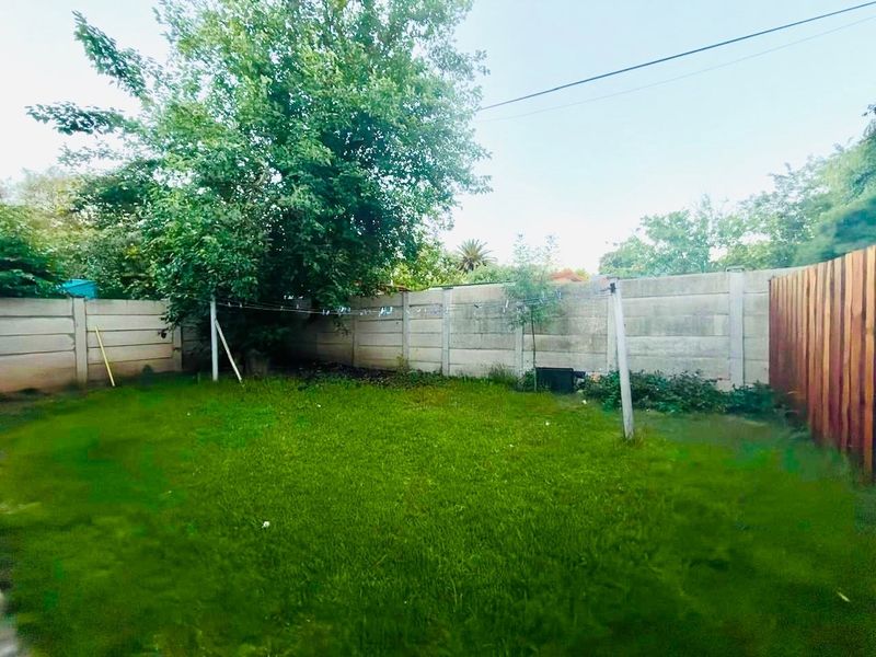 A private backyard garden featuring a lawn, mature tree, and a combination of precast concrete and wooden boundary fencing.