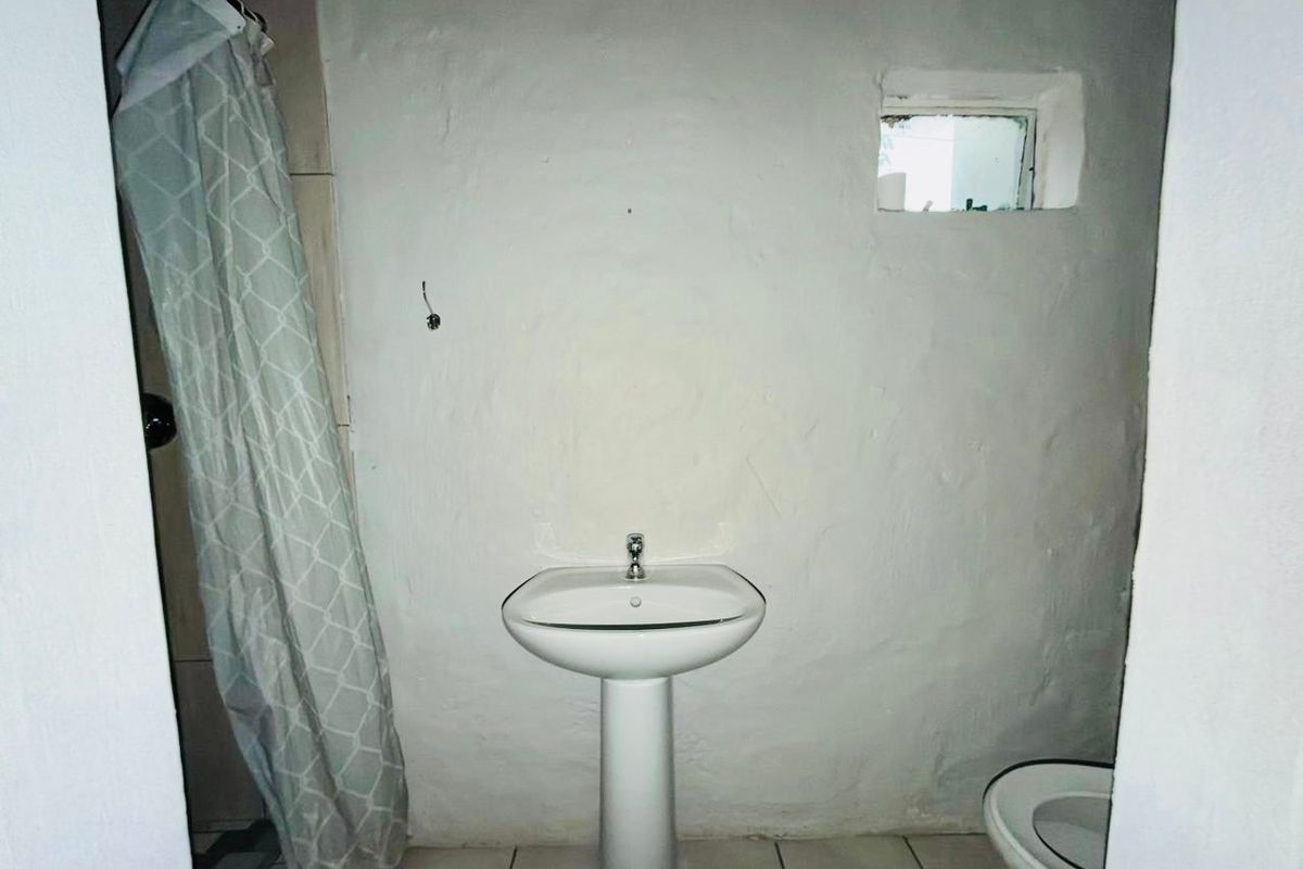 A compact bathroom featuring a pedestal basin, toilet, and shower area with tiled flooring and a small window.