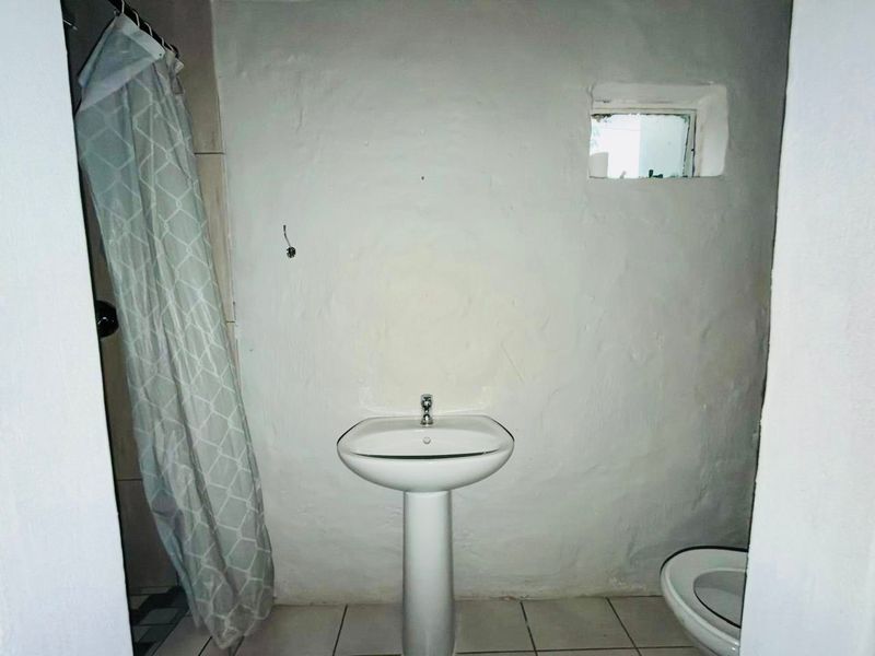 A compact bathroom featuring a pedestal basin, toilet, and shower area with tiled flooring and a small window.