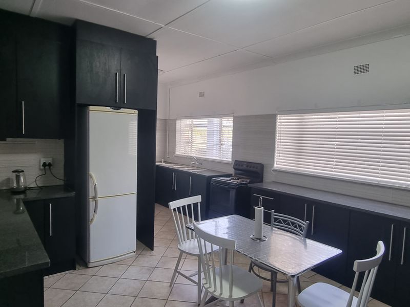 A functional kitchen featuring dark cabinetry, laminate countertops, a freestanding stove, and tiled flooring, offering a practical layout with ample natural light.