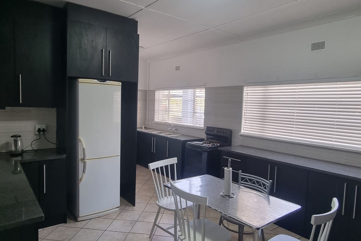 A functional kitchen featuring dark cabinetry, laminate countertops, a freestanding stove, and tiled flooring, offering a practical layout with ample natural light.