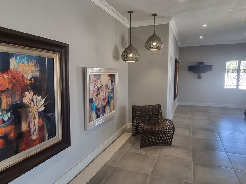 A spacious hallway featuring neutral grey walls, large format floor tiles, decorative pendant lighting, and crown molding details.
