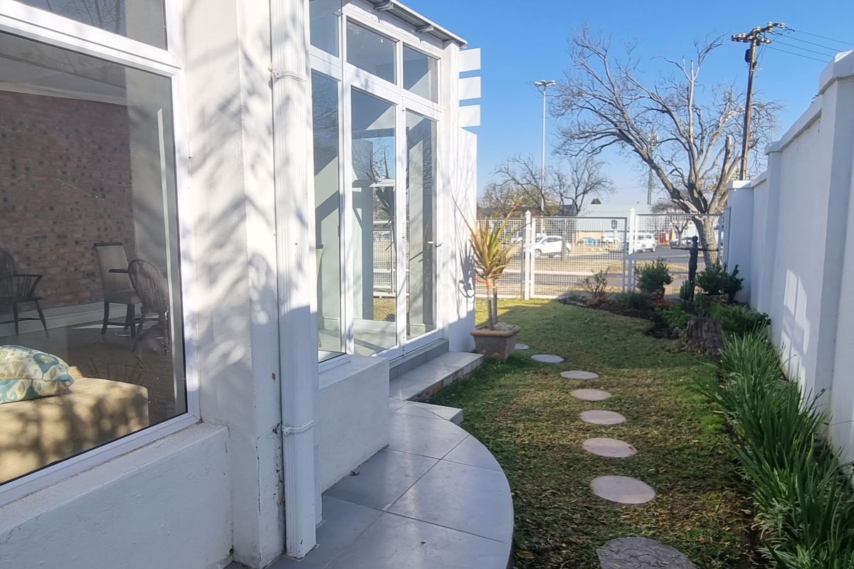 A view of the rear exterior featuring a tiled patio area, large glass doors, and a landscaped garden with a stone pathway.