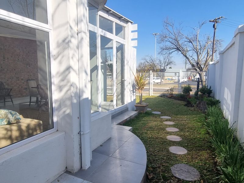 A view of the rear exterior featuring a tiled patio area, large glass doors, and a landscaped garden with a stone pathway.