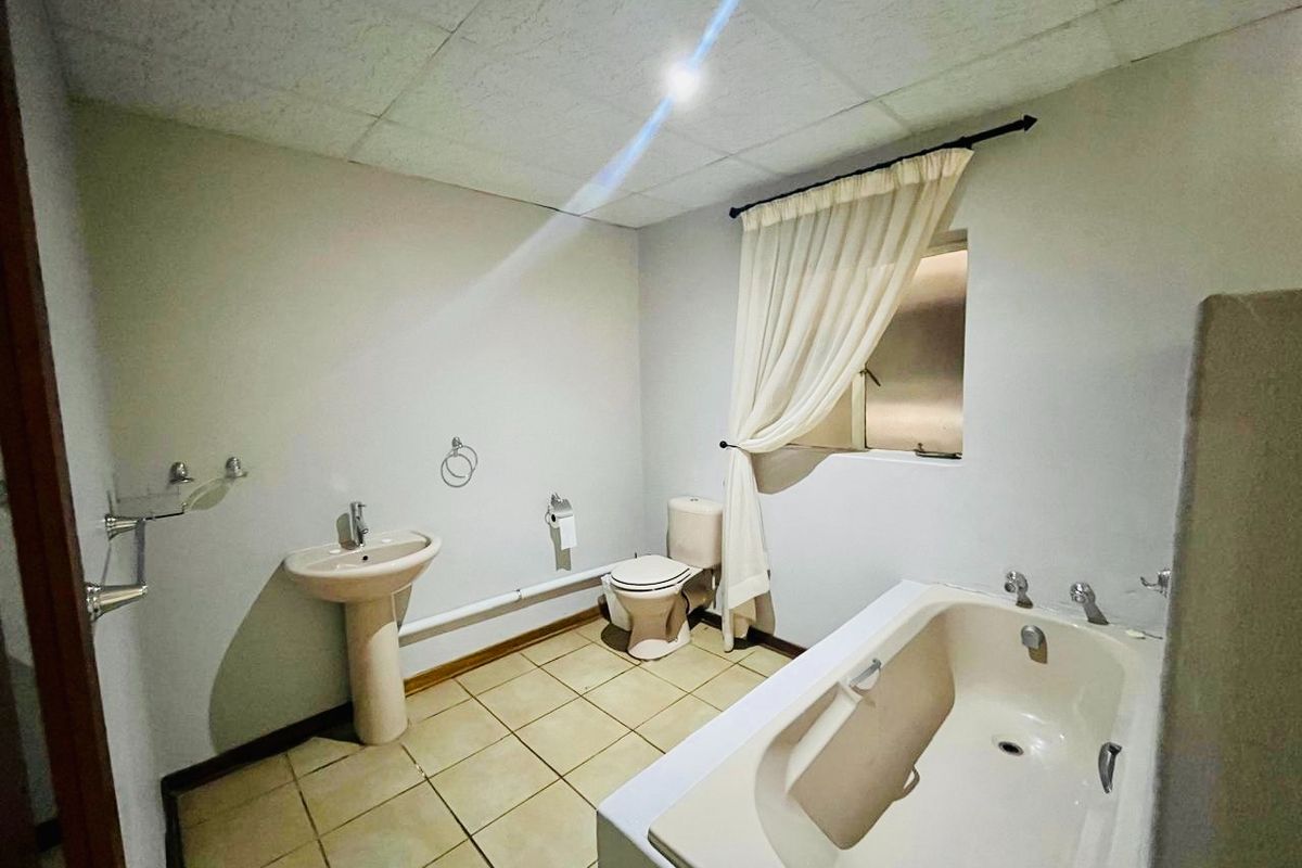 A functional bathroom featuring a pedestal sink, toilet, and built-in bathtub with tiled flooring and a drop ceiling.