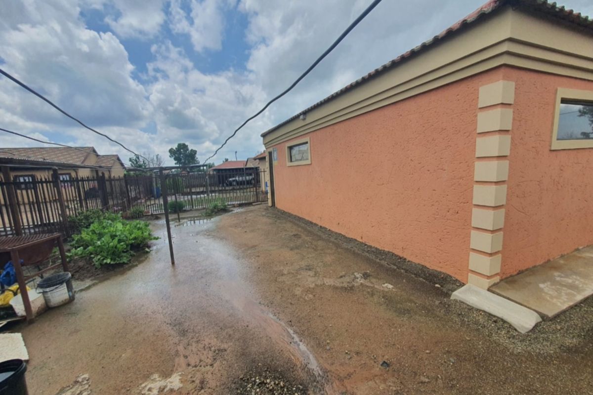 Exterior view of the side of the house showing a muddy yard area with poor drainage and perimeter fencing.
