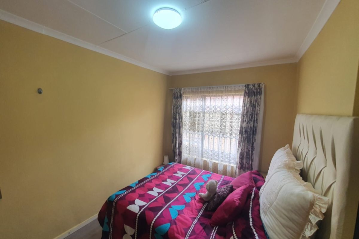 A standard bedroom featuring neutral wall tones, a window with curtain fixtures, and a ceiling-mounted light fitting.