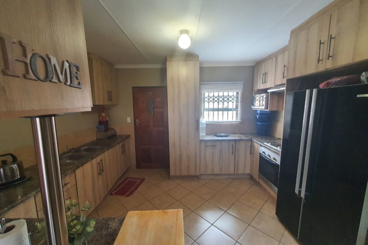 A functional kitchen featuring light wood-look cabinetry, granite-style countertops, tiled flooring, and a built-in oven with extractor fan.