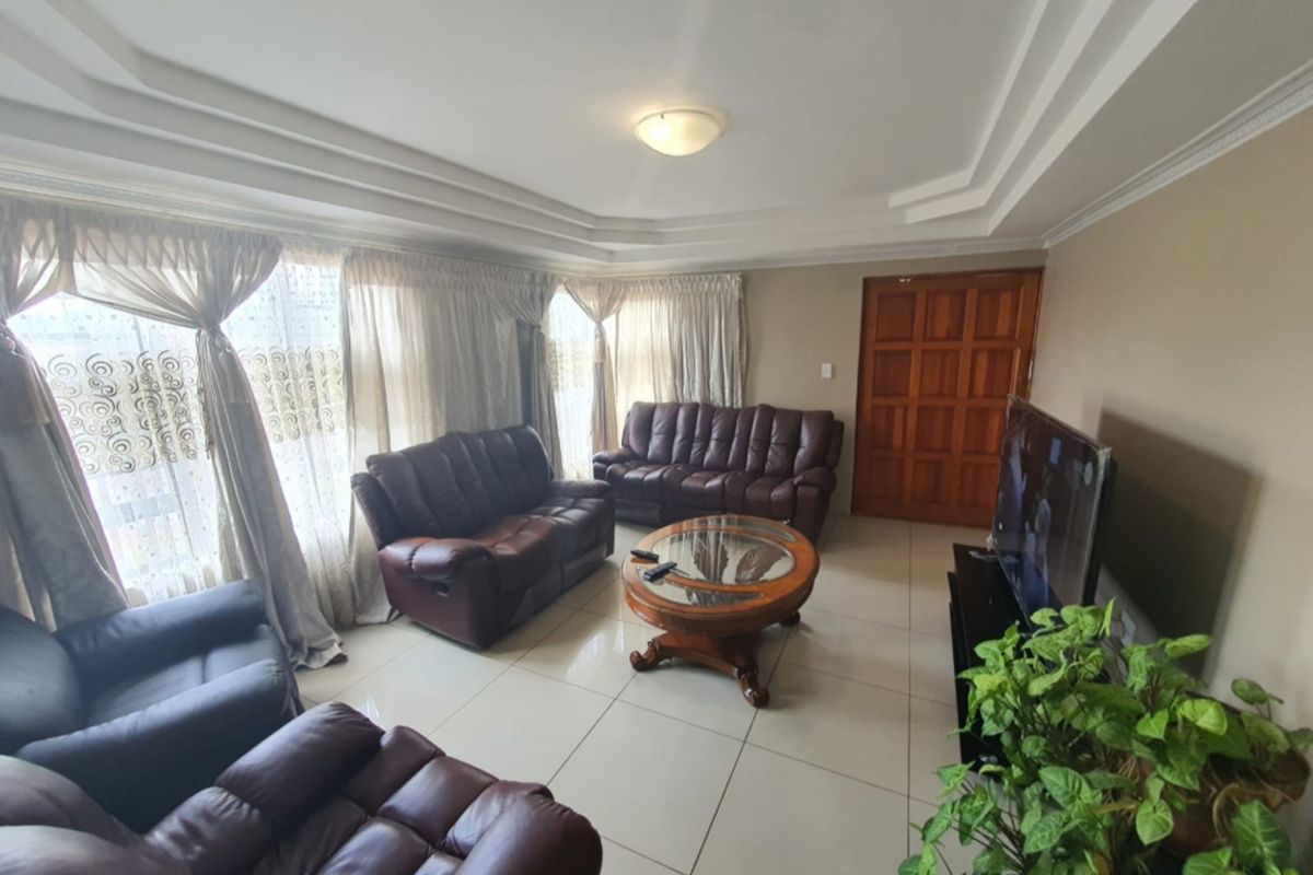 A spacious living room featuring large format floor tiles, a decorative tray ceiling, and a solid timber panel door.