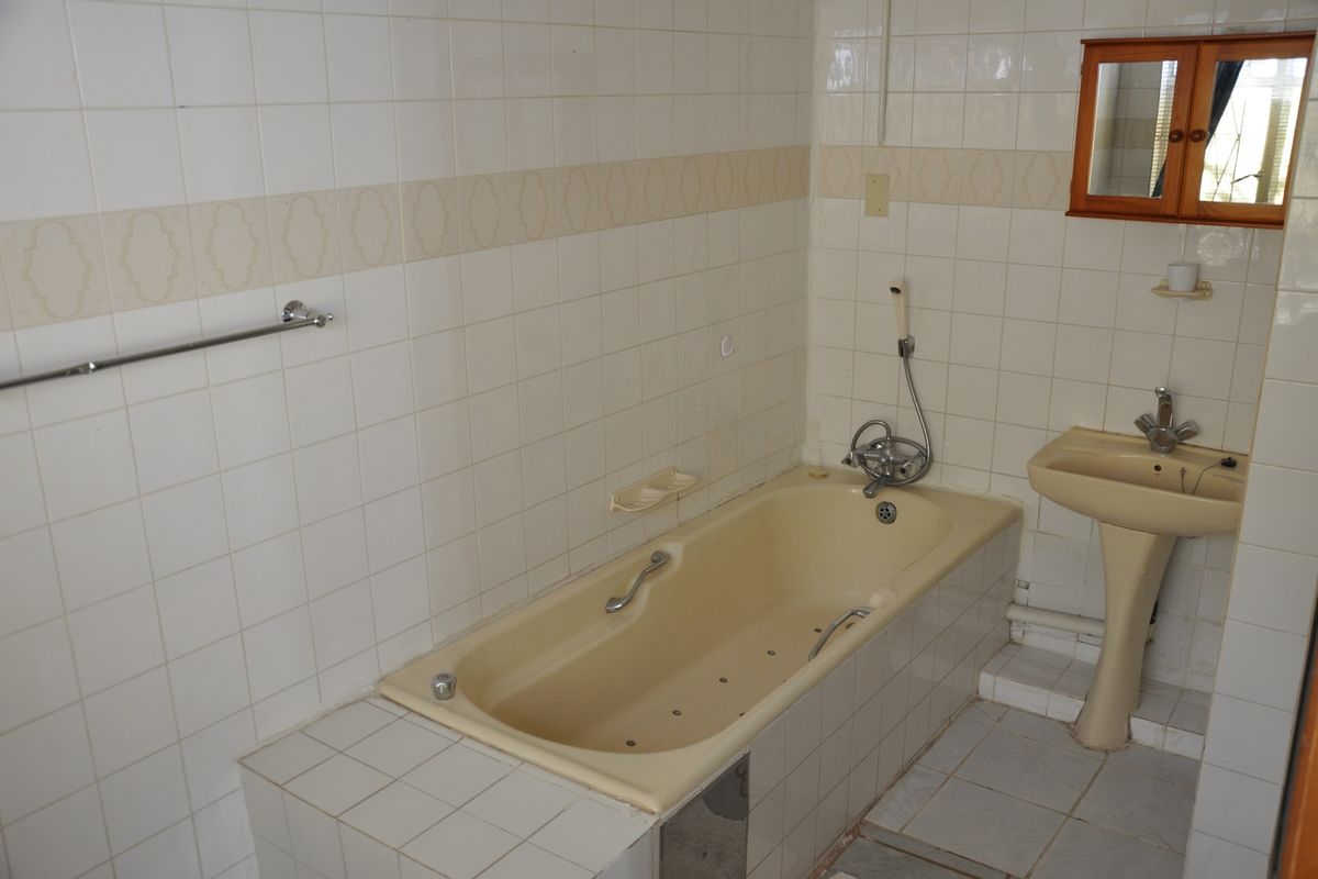 A dated bathroom featuring a built-in bathtub, pedestal sink, and wall-mounted medicine cabinet with full-height wall tiling.