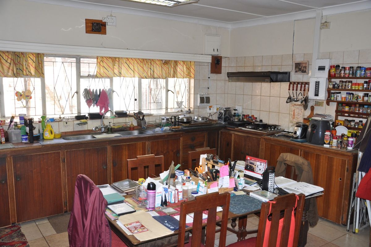 A dated kitchen featuring wooden cabinetry, tiled splashbacks, a built-in extractor fan, and a double sink, offering significant potential for modernization and renovation.