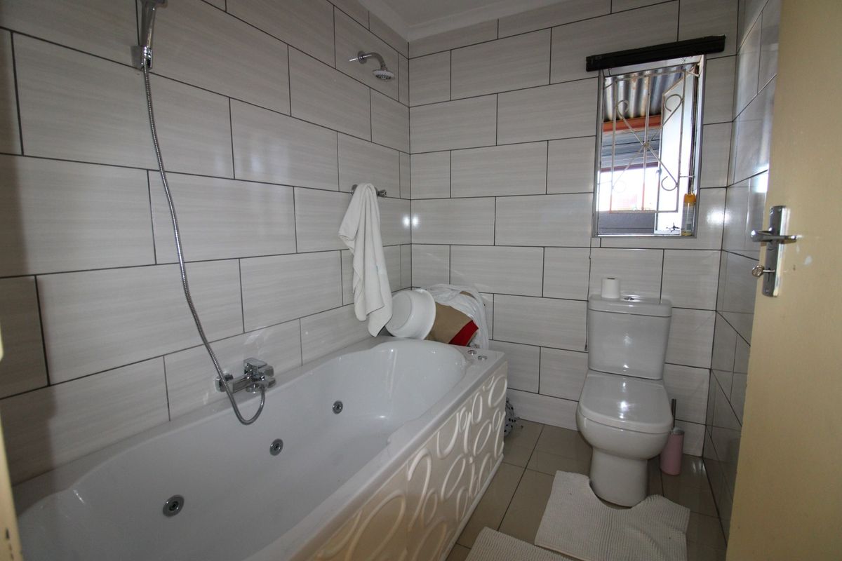 A functional bathroom featuring a jetted bathtub with handheld shower attachment, a standard toilet, and full-height wall tiling.