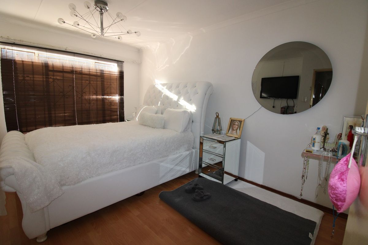 A bedroom featuring laminate flooring, a large window with fitted blinds, and a modern ceiling light fixture.