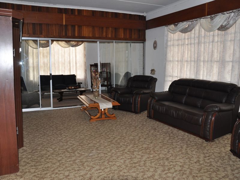 Spacious living area featuring wood-paneled wall accents, carpeted flooring, and large sliding glass doors leading to an adjacent sunroom or patio space.