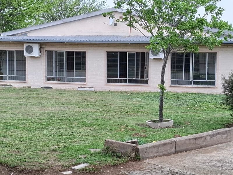 Rear view of a single-story brick farmhouse featuring a metal roof, security-barred windows, and dual air conditioning units overlooking a spacious lawn.