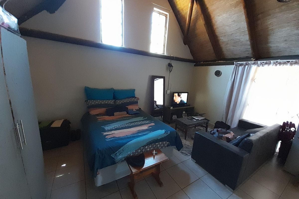 Spacious bedroom featuring high vaulted ceilings with exposed timber beams, tiled flooring, and large windows providing natural light.