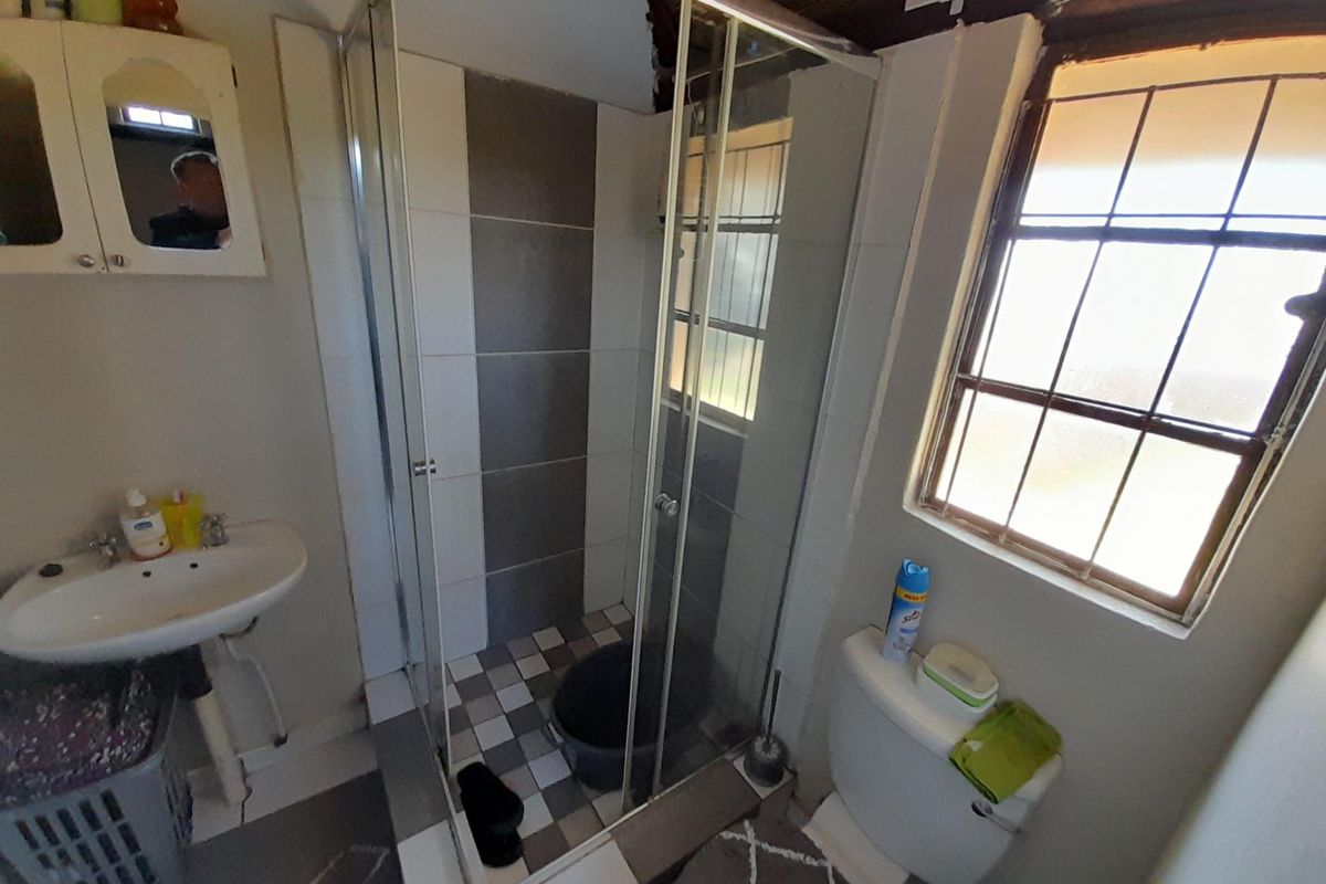 Compact bathroom featuring a glass-enclosed shower, pedestal basin, and toilet, with a window providing natural light.