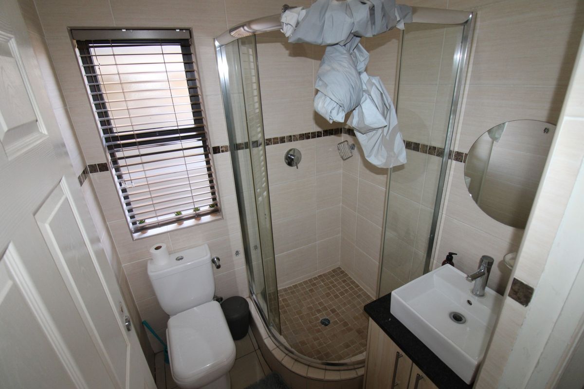 Compact bathroom featuring a corner shower enclosure, modern vanity with basin, and a standard toilet, finished with neutral wall tiles.