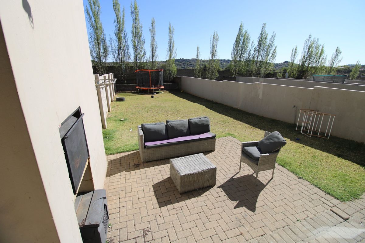 A private rear garden featuring a paved patio area with a built-in braai, overlooking a lawned yard enclosed by perimeter walls.