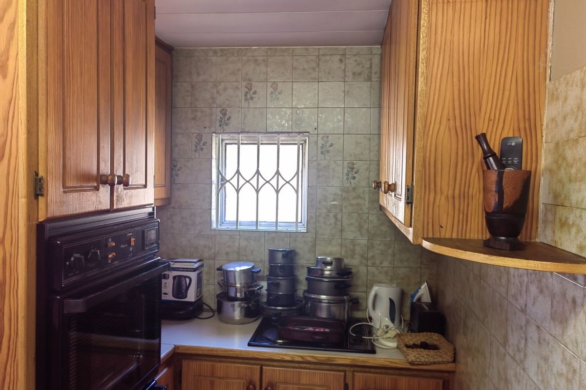 A compact kitchen featuring wooden cabinetry, a built-in oven, and a hob, with a window protected by security bars.