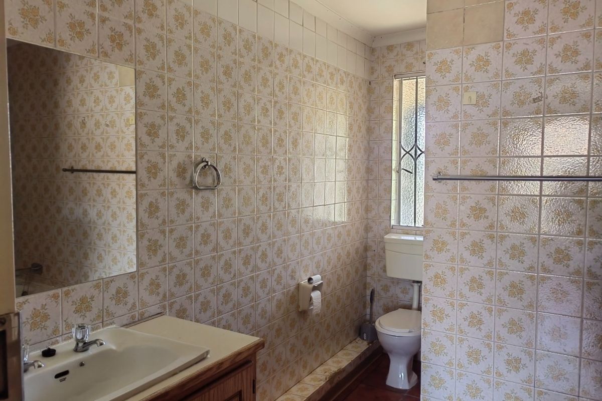 A dated bathroom featuring original floral wall tiles, a built-in vanity with basin, and a standard toilet suite.
