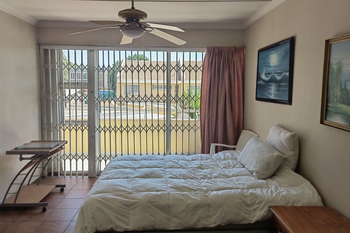 A bedroom featuring tiled flooring, a ceiling fan, and a sliding glass door with a security gate leading to an outdoor area.