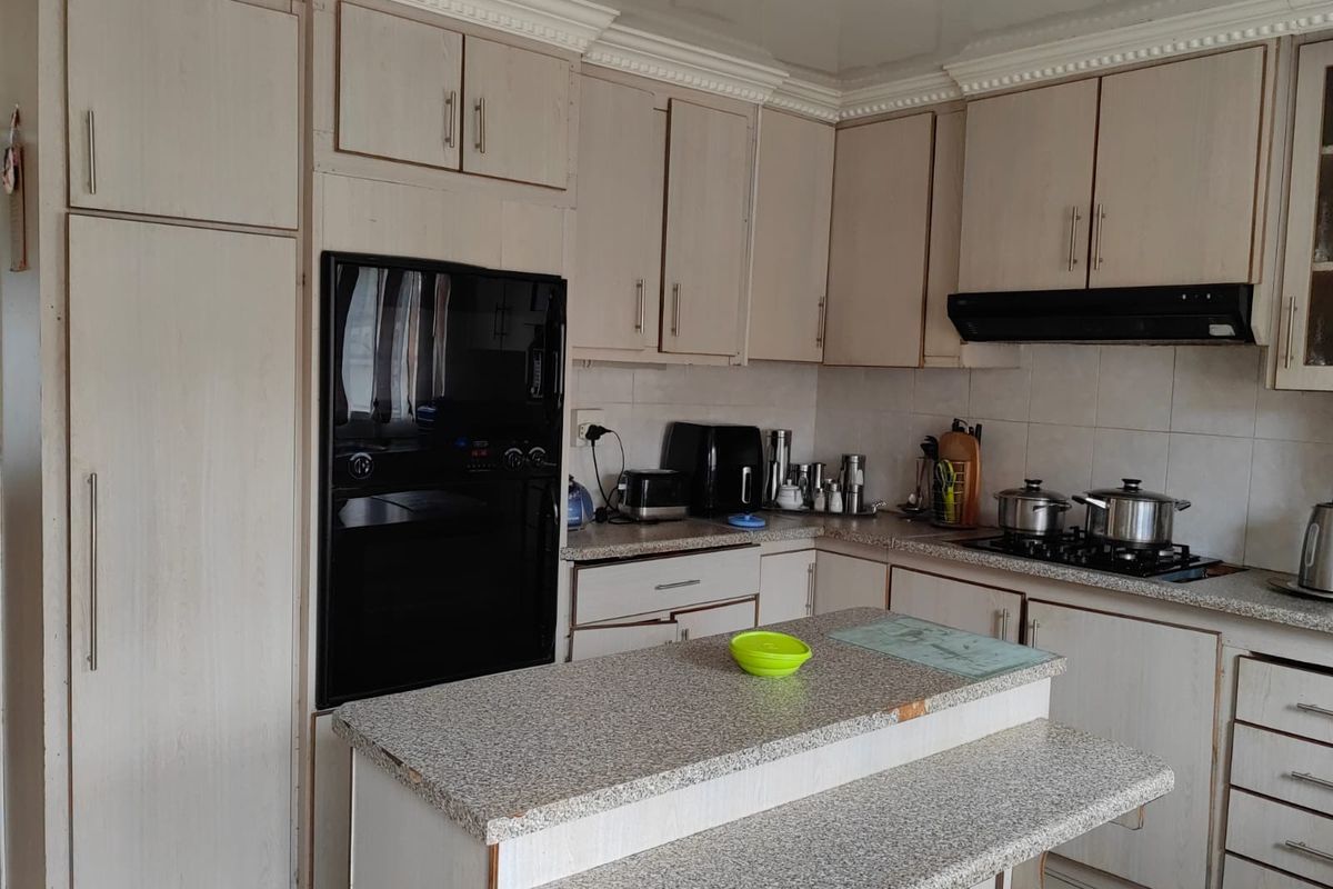 Functional kitchen featuring light-toned cabinetry, built-in oven, gas hob with extractor fan, and a central island with stone-look laminate countertops.