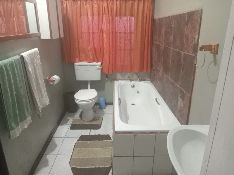 A functional bathroom featuring a standard bathtub with tiled surround, a toilet, and a pedestal basin, finished with ceramic floor tiles.