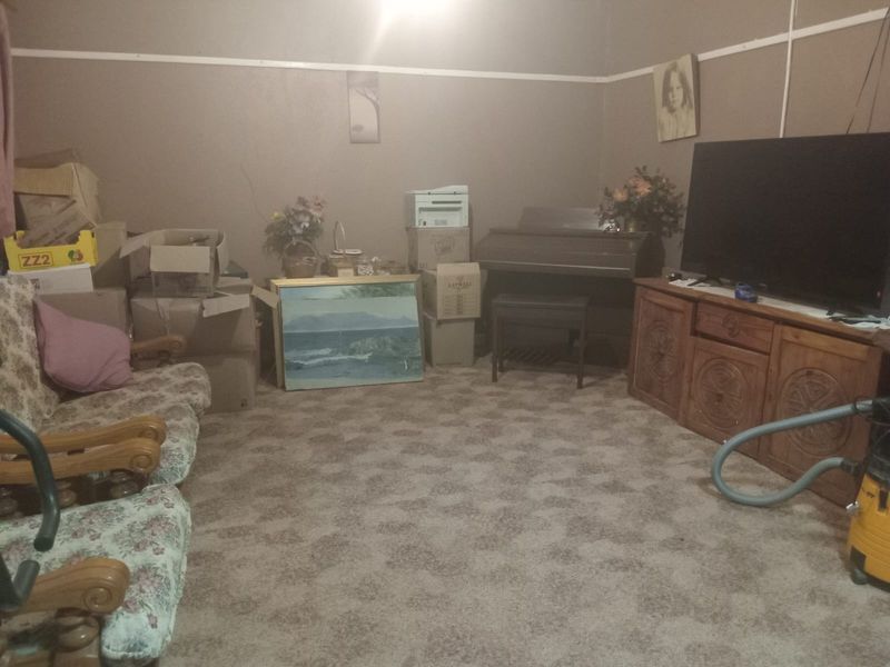 A living room space featuring wall-to-wall carpeting and neutral wall finishes, currently used as a storage and living area.