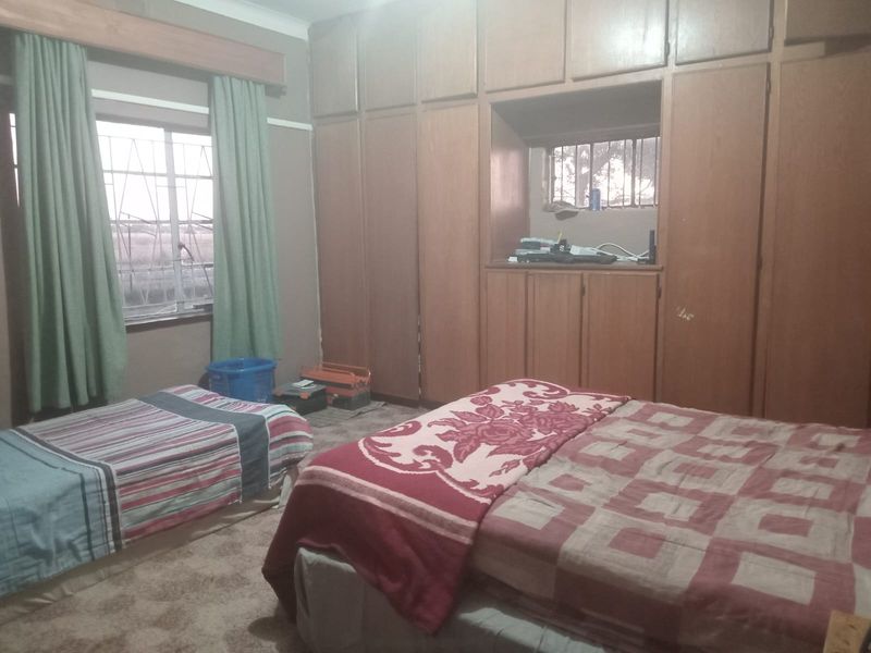 A bedroom featuring extensive built-in wooden cabinetry and a window with security bars, offering functional storage space in a dated interior setting.