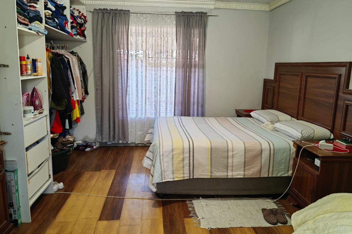 A bedroom featuring wood-look laminate flooring, crown molding, and a built-in wardrobe unit with open shelving.