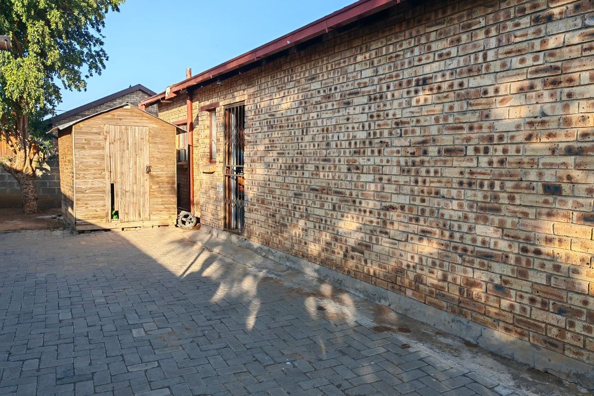 Rear exterior view of the property featuring face-brick walling, paved courtyard area, and a detached timber storage shed.